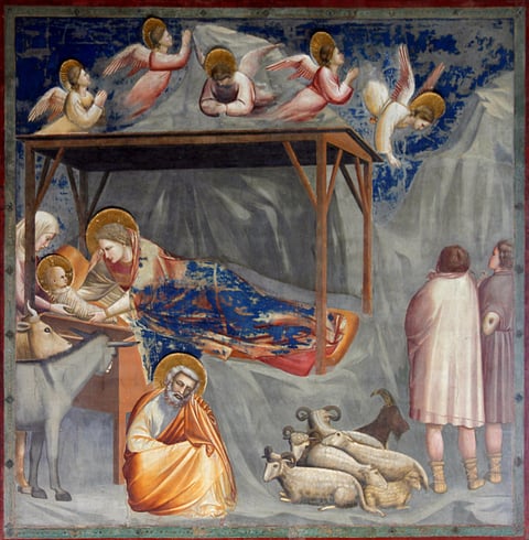 Giotto’s The Nativity fresco: Mary lies under a wooden shelter with the swaddled baby, Joseph sits below, and shepherds, animals and angels gather under a blue sky.